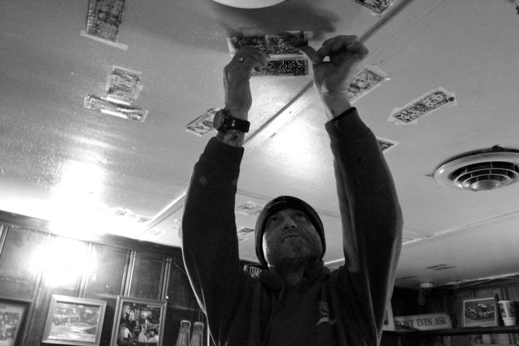 Pungo resident Herb Smith, 50, tapes a dollar bill bearing the names of his sons on the ceiling. He’s come to Monk’s since he was five, when his father brought him in. [John-Henry Doucette/The Princess Anne Independent News]