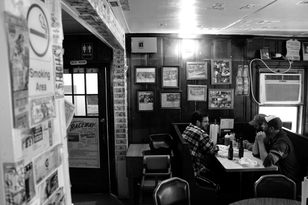 Alex D’Angelo, 30, and brothers Adam Krabiel, 37, and Kyle Krabiel, 35, enjoy a meal near pillars showing columns of currency.  [John-Henry Doucette/The Princess Anne Independent News]