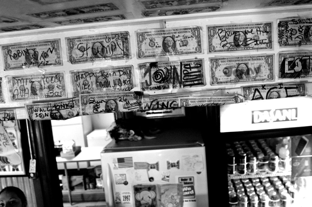Dollars bearing messages adorn the wall and ceiling above a counter at Monk’s Place, a Creeds institution. At bottom left, Ashley Johnson delivers an order. She has three dollars posted herself. [John-Henry Doucette/The Princess Anne Independent News]