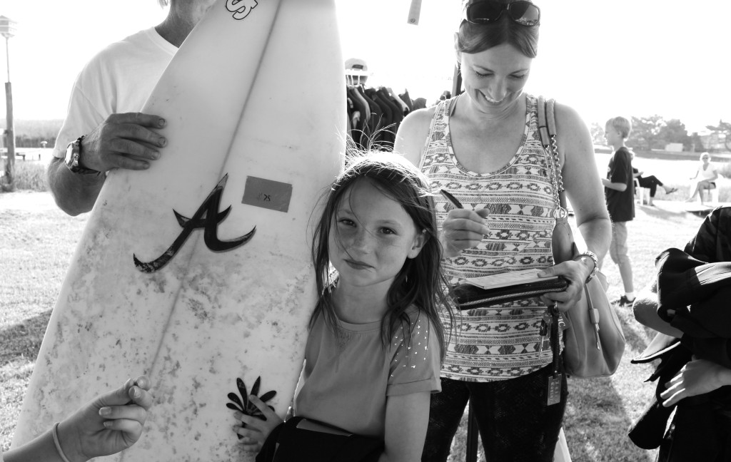 Lago Mar’s Ava Heil, 8, holds a board while her mom, Suzy Heil, writes a check at the recent Sandbridge swap meet. [John-Henry Doucette/The Princess Anne Independent News]
