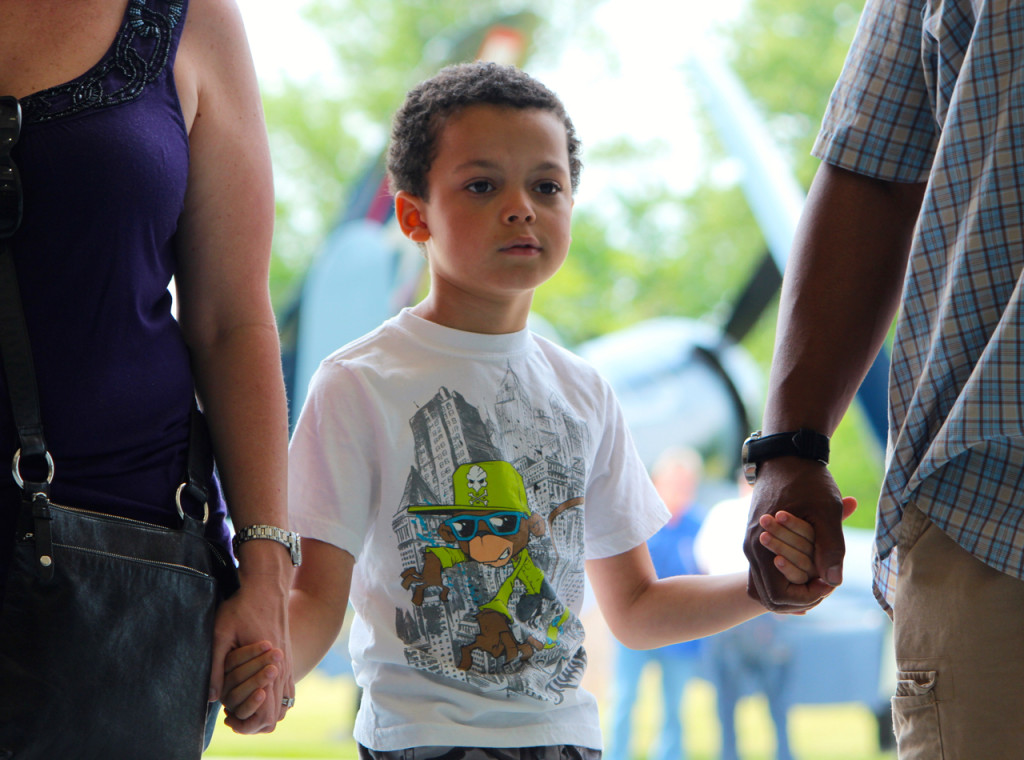 With a warbird behind him and holding the hands of loved ones, Aiden Brown, 7, takes in the sights at the Warbirds Over the Beach air show on Saturday, May 16, at the Military Aviation Museum. [John-Henry Doucette/The Princess Anne Independent News]