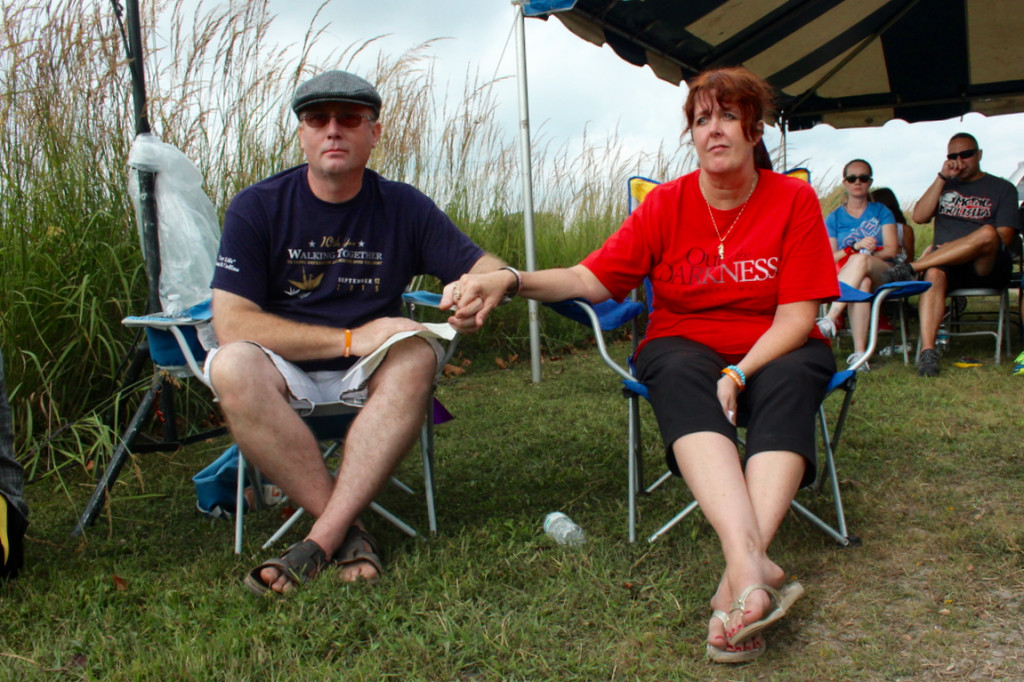 Steve and Kym Bach hold hands while names are read during a ceremony before the Out of the Darkness Community Walk at Mount Trashmore on Saturday, Sept. 12. The Bachs were among the speakers. [John-Henry Doucette/The Princess Anne Independent News]