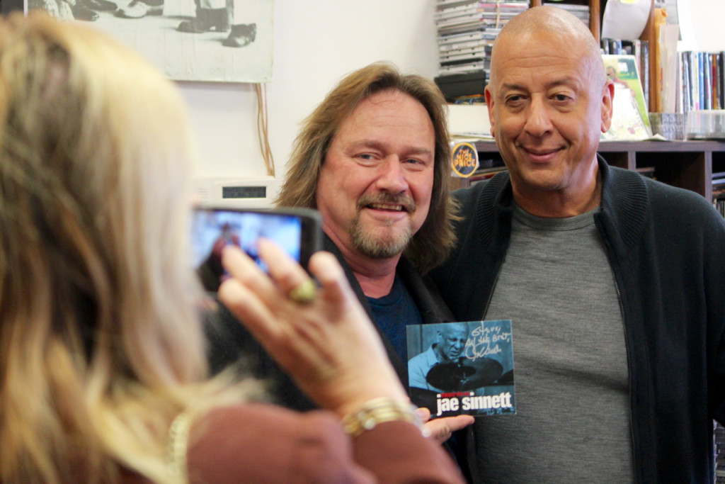 Musician Steve Archer poses with Jae Sinnett and an autographed copy of Zero to 60 while Steve Archer’s wife, Sandy Archer, snaps a photo at Birdland Music. [John-Henry Doucette/The Princess Anne Independent News]