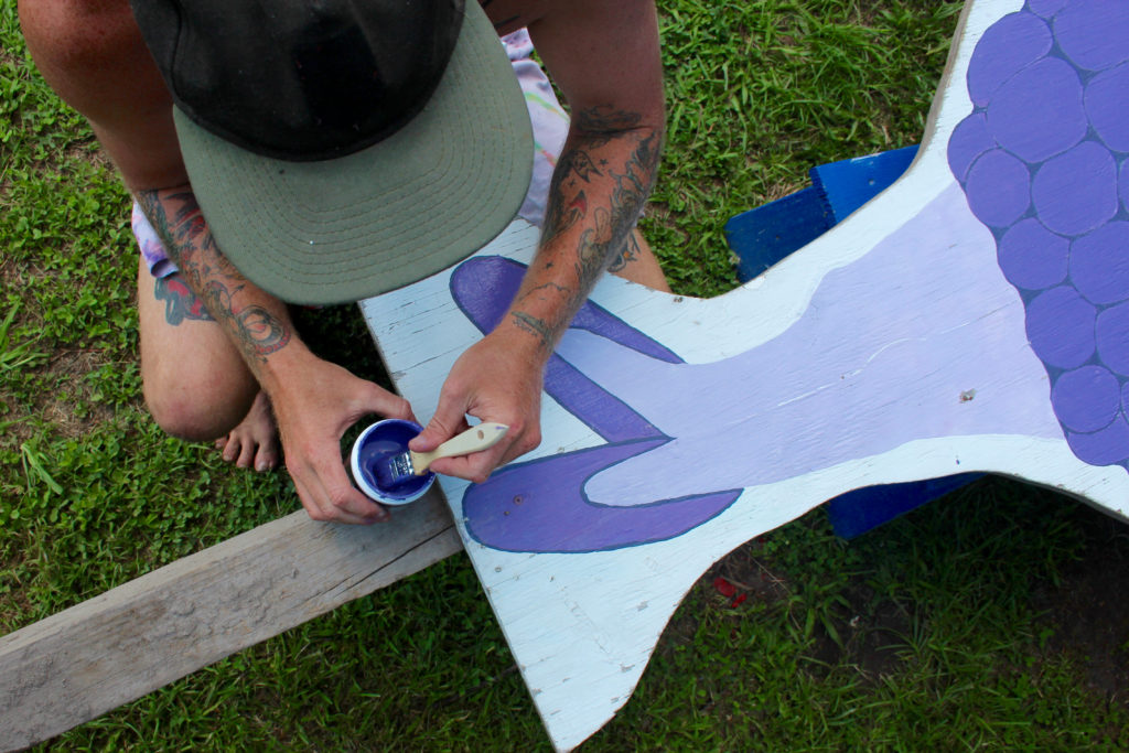 Farmhand Max Aaron, 24, of Red Mill, refreshes the paint on a sign at Pungo Blueberries, Etc., which recently opened for the summer season. [John-Henry Doucette/The Princess Anne Independent News]