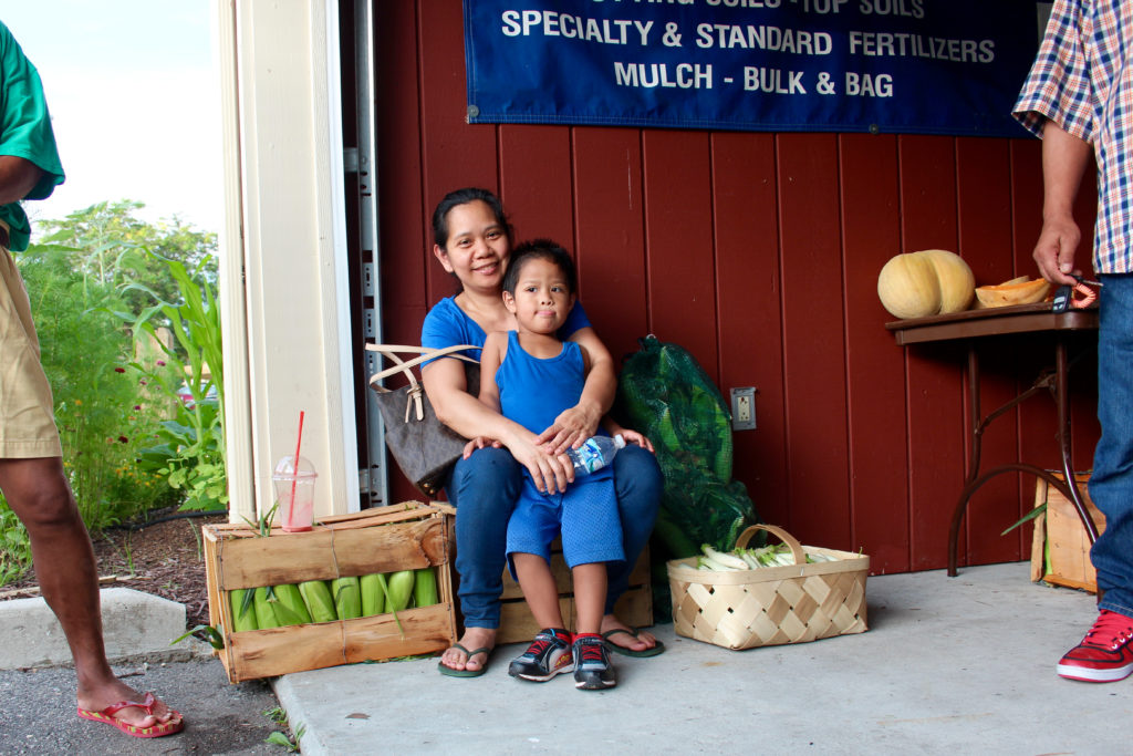 Maritess Caalim, seen with her son, Alexis, 3, visited the market while visiting family. Her brother-in-law, Mario Caalim of Virginia Beach, often comes to the market, and he said he was buying corn and other produce to cook for his loved ones while they visited. “I come here almost always,” he said. “The price is good.” [John-Henry Doucette/The Princess Anne Independent News]