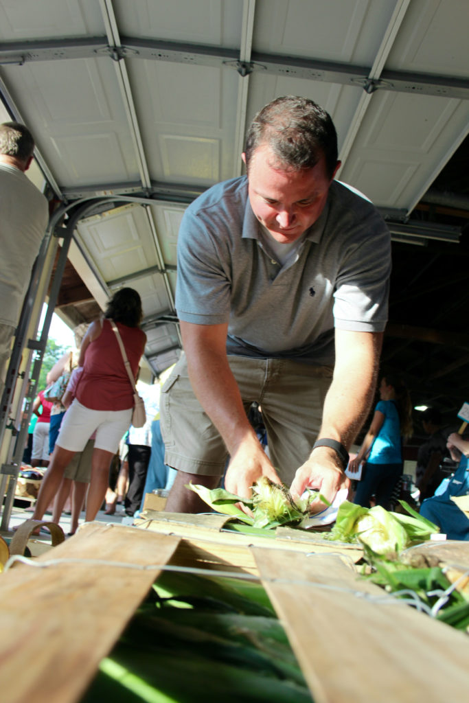 Troy Barnes, 44, of Suffolk, opens an ear of his bicolor sweet corn so bidders can have a look at its yellow and white kernals. Barnes decided to bring some produce for the auction, and he also meant to buy produce while he was there. [John-Henry Doucette/The Princess Anne Independent News]