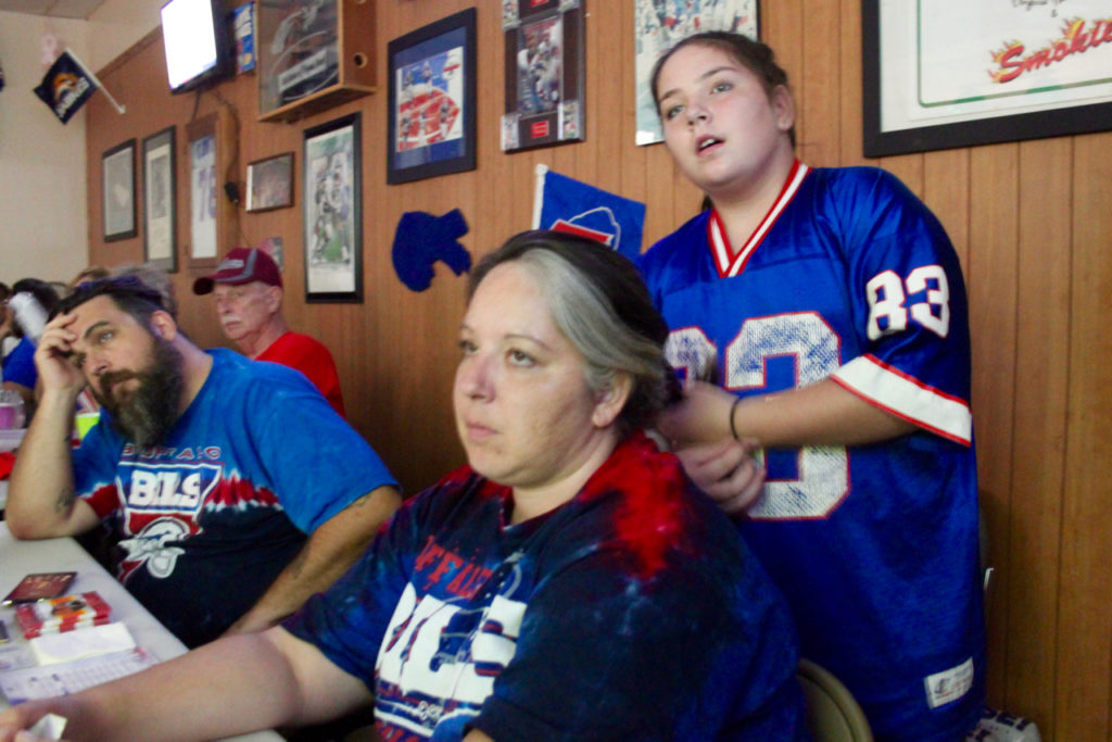 Chris and Alana Litz watch a tough fourth quarter for the Bills while daughter Leah Harris, 11, works on mom’s hair. [John-Henry Doucette/The Princess Anne Independent News]