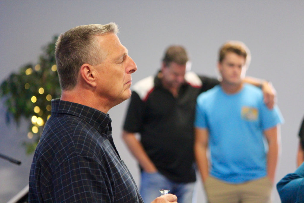 The Rev. Kevin Milcarek, pastor of Back Bay Christian Assembly, is seen amid prayer during a service on Sunday, Sept 11. The congregation is in its 30th year. In the background are John Murphy, who has his arm around his son, Dylan Murphy, 17 [John-Henry Doucette/The Princess Anne Independent News]