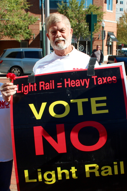 City Treasurer John Atkinson and opponents of extending light rail to Town Center brought signs and flowers to a rally held by their opposition. [John-Henry Doucette/The Princess Anne Independent News]