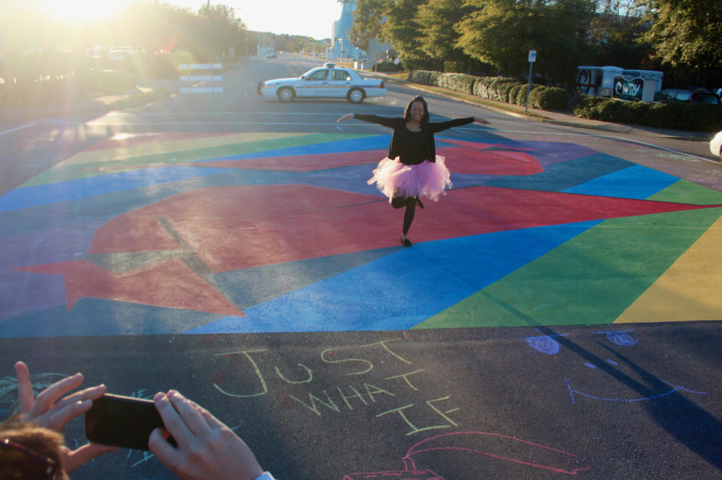 Natasha Johnson, a 30-year-old college student who also works as a server at Croc’s 19th Street Bistro, poses for a picture at the painting at the intersection of 19th Street and Cypress Avenue, a community “paint the pavement” project in the ViBe Creative District. [John-Henry Doucette/The Princess Anne Independent News]